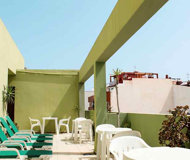 Terassi aurinkotuoleilla ja pöydillä, vihreiden seinien ympäröimänä. (Tekoälyn luoma teksti)