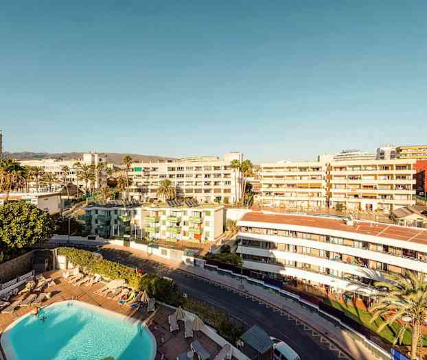 Näkymä hotellialueelle, jossa uima-allas ja ympärillä rakennuksia kirkkaan taivaan alla. (Tekoälyn luoma teksti)