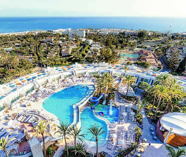 Lentokuva suuresta lomakohteesta, jossa uima-allasalue ja palmuja ympärillä. (Tekoälyn luoma teksti)