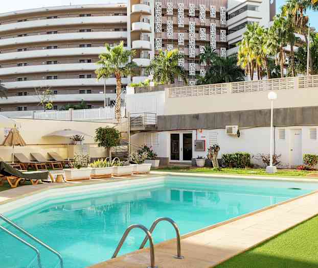 Ulkoallas, jota ympäröivät aurinkotuolit, kasvillisuus ja rakennus taustalla. (Tekoälyn luoma teksti)