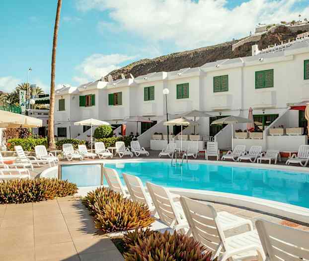 Uima-allasalue aurinkotuoleilla ja varjoilla valkoisen talon edessä, jossa on vihreät ikkunaluukut. (Tekoälyn luoma teksti)