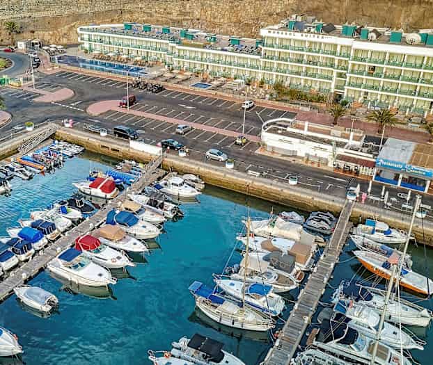 Ilmakuva satamasta, jossa veneitä on pysäköity rakennusten ja pysäköintialueen edessä. (Tekoälyn luoma teksti)