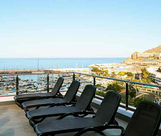 Kuva terassista, jossa on aurinkotuoleja ja näkymä satamaan ja merelle. (Tekoälyn luoma teksti)