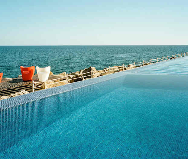 Infinitiiallas, josta on näkymä rauhalliselle merelle, sekä puisella terassilla värikkäitä tuoleja. (Tekoälyn luoma teksti)