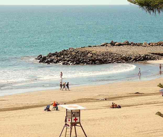 Ranta uimareiden, pelastustornin ja kallioiden kanssa meren äärellä. (Tekoälyn luoma teksti)