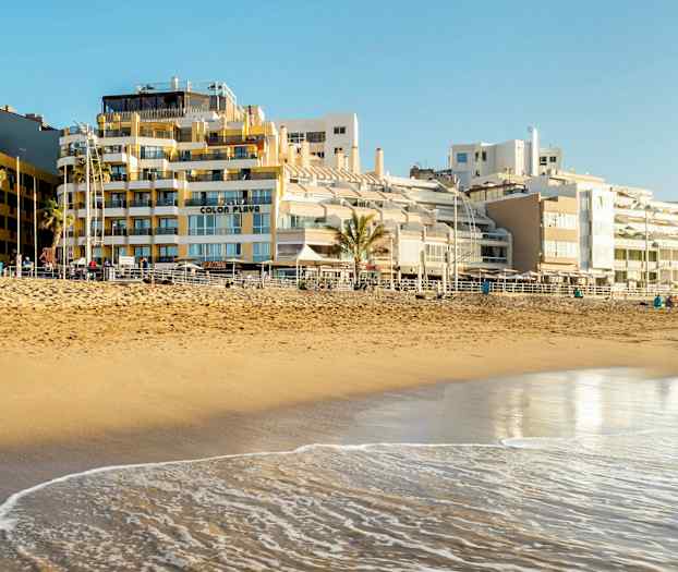 Hiekkaranta meren äärellä, taustalla rakennuksia. (Tekoälyn luoma teksti)