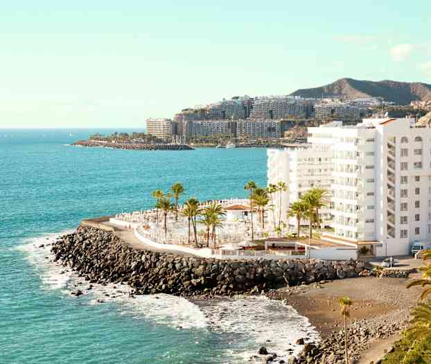 Valkoinen rakennus kivisellä rannikolla, taustalla palmuja ja meri. (Tekoälyn luoma teksti)