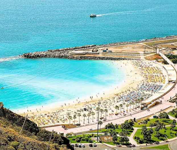 Ranta, jossa on valkoista hiekkaa ja sinistä vettä rantaviivalla, jossa on aurinkotuoleja ja sateenvarjoja. (Tekoälyn luoma teksti)