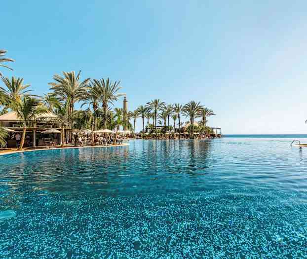 Suuri uima-allas, jota ympäröivät palmut ja sininen taivas, taustalla meri. (Tekoälyn luoma teksti)