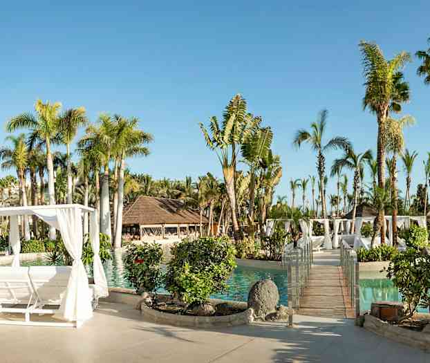 Aurinkoinen lomakeskus, jossa uima-allas, palmuja, puurakenteinen pergola ja istutuksia. (Tekoälyn luoma teksti)