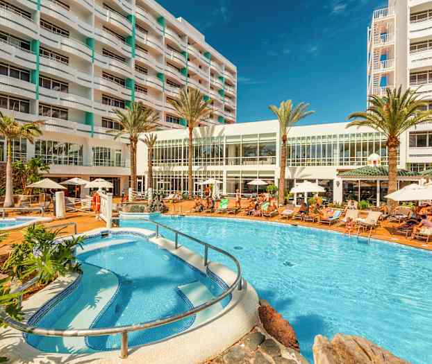 Hotellialue, jossa uima-allas, aurinkotuoleja ja rakennus taustalla. (Tekoälyn luoma teksti)