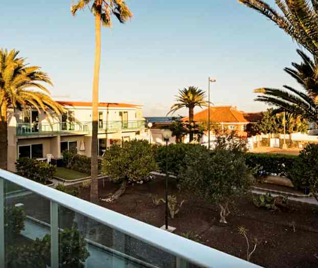 Ulkomaisema, jossa on palmuja ja asuinrakennuksia taustalla, kuvattu parvekkeelta. (Tekoälyn luoma teksti)