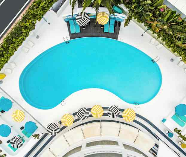 Ilmakuva allasalueesta, jossa on aurinkotuoleja ja värikkäitä aurinkovarjoja. (Tekoälyn luoma teksti)