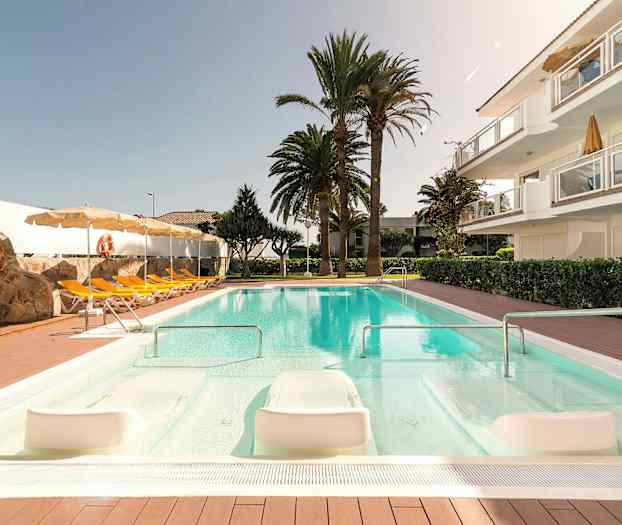 Uima-allasalue aurinkotuoleilla, päivänvarjoilla, kiviseinällä ja ympäröivillä puilla. (Tekoälyn luoma teksti)