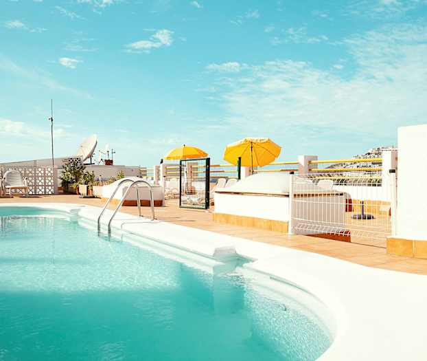 Ulkoallas, jossa turkoosia vettä, ympärillä aurinkoterassi ja keltaisia aurinkovarjoja. (Tekoälyn luoma teksti)