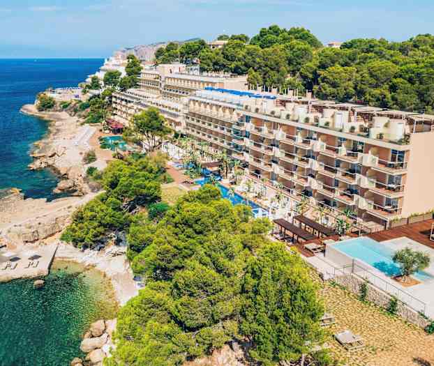 Monikerroksinen hotelli rannalla, jossa edessä uima-allas ja ympärillä kasvillisuutta. (Tekoälyn luoma teksti)