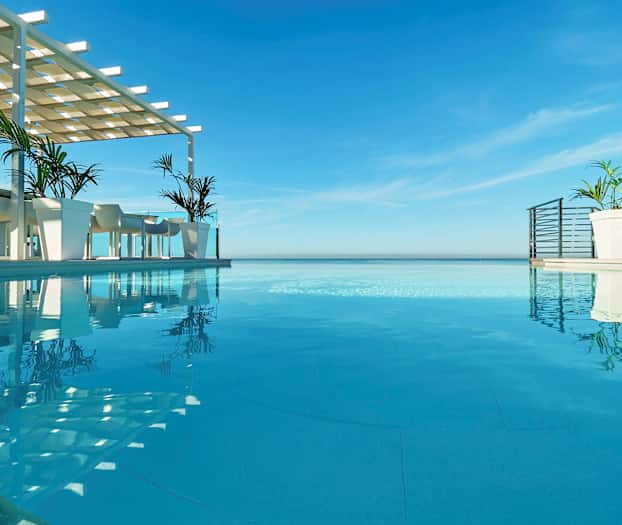 Ääretön uima-allas merinäköalalla, pöytiä ja tuoleja katosrakennelman alla altaan vieressä. (Tekoälyn luoma teksti)