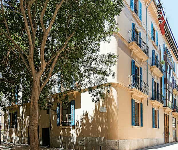 Rakennus, jossa on useita parvekkeita ja sinisiä ikkunaluukkuja. (Tekoälyn luoma teksti)