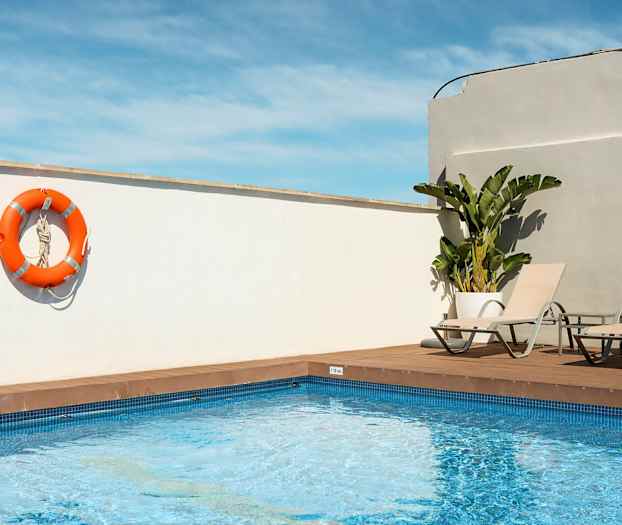 Ulkouima-allas, jossa kaksi aurinkotuolia ja oranssi pelastusrengas roikkuu valkoisella seinällä. (Tekoälyn luoma teksti)