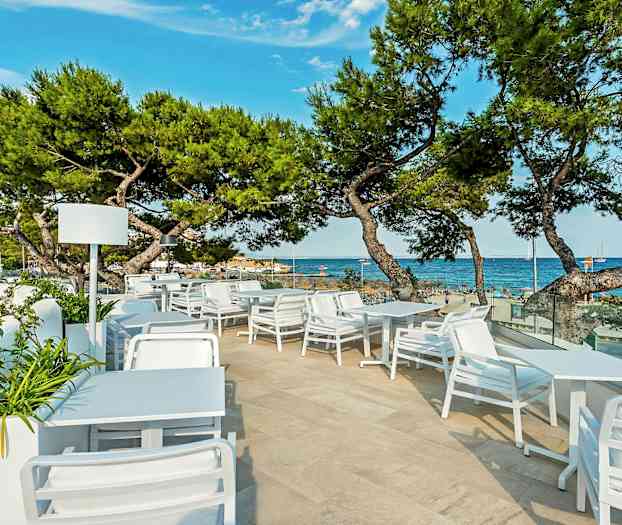 Ulkoilmaravintola, jossa valkoiset huonekalut ja näkymä merelle ja rannalle. (Tekoälyn luoma teksti)