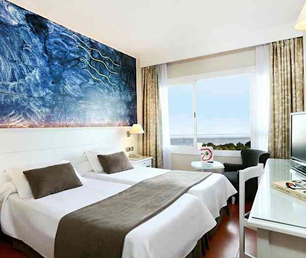 Hotellihuone, jossa kaksi erillistä vuodetta valkoisilla vuodevaatteilla ja ruskeilla peitteillä, seinällä taiteellinen maalaus ja ikkuna, josta on merinäköala. (Tekoälyn luoma teksti)