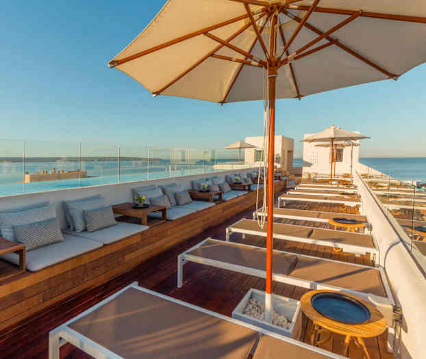 Näkymä modernille kattoterassille, jossa aurinkotuoleja ja varjoja, kohti merta. (Tekoälyn luoma teksti)