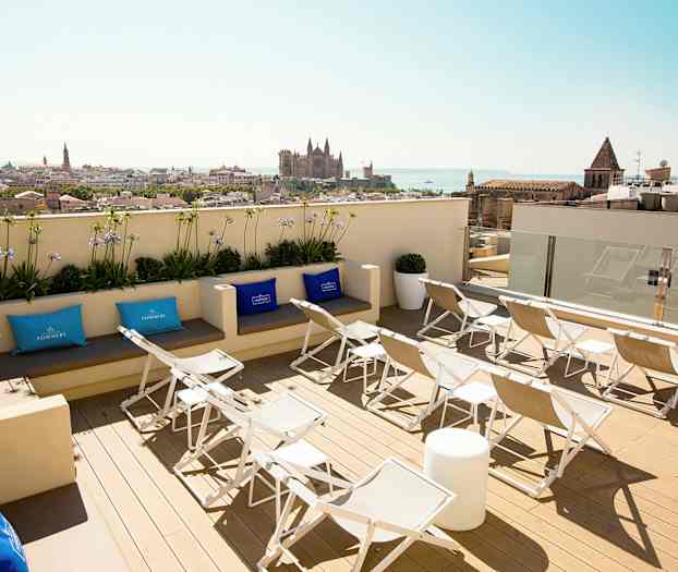 Näkymä kattoterassilta, jossa on aurinkotuoleja ja istumapaikkoja, taustalla kaupunki ja sen katedraali. (Tekoälyn luoma teksti)