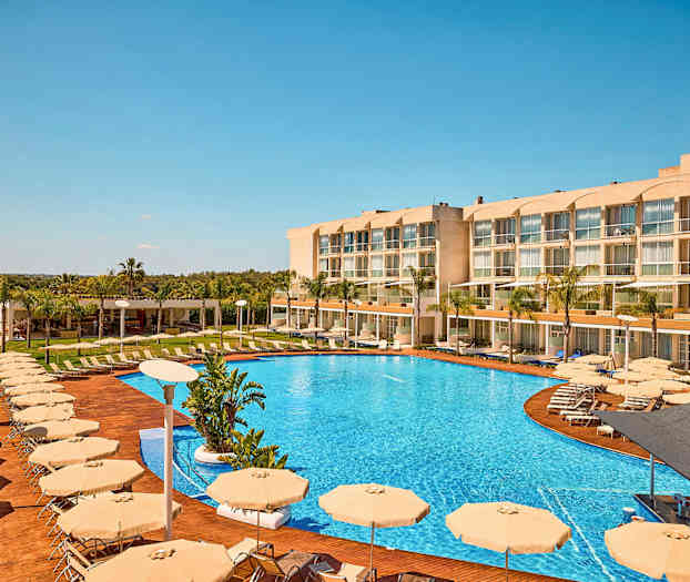 Kuva hotellista, jossa on suuri uima-allas, aurinkotuoleja ja aurinkovarjoja. (Tekoälyn luoma teksti)