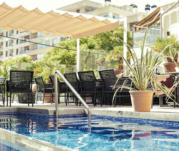 Istuma-alue, jossa mustat huonekalut, altaan vieressä, jossa siniset laatat, ympäröity ruukkukasveilla. (Tekoälyn luoma teksti)