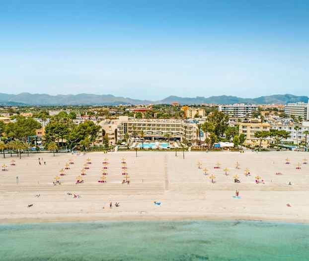 Ranta aurinkotuoleineen ja -varjoineen, hotelli ja kaupungin siluetti taustalla. (Tekoälyn luoma teksti)