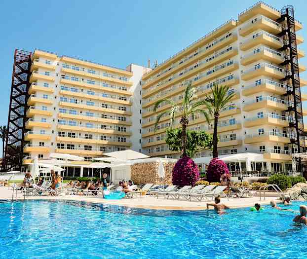 Kuva hotellista, jossa on useita kerroksia, sekä ulkouima-allas, jossa ihmiset uivat ja rentoutuvat. Altaan ympärillä on palmuja ja kukkia. (Tekoälyn luoma teksti)