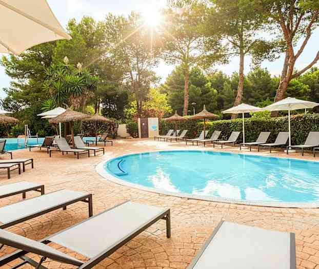 Aurinkotuoleja uima-altaan äärellä, aurinkovarjoja ja puita taustalla. (Tekoälyn luoma teksti)