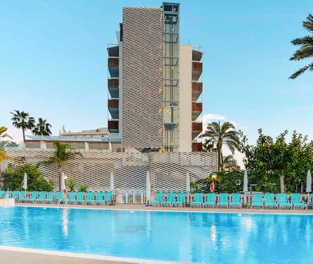 Rakennus, jonka edessä on uima-allas sekä palmuja ja aurinkotuoleja. (Tekoälyn luoma teksti)