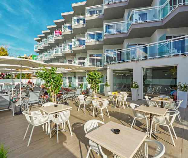 Ulkotila, jossa on pöytiä ja tuoleja sekä aurinkotuoleja hotellin parvekkeiden edessä. (Tekoälyn luoma teksti)