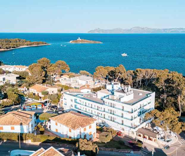 Lentokuva rannikkoalueesta, rakennuksia, rannan lähellä olevia taloja ja merinäköala, jossa taustalla pieni saari. (Tekoälyn luoma teksti)