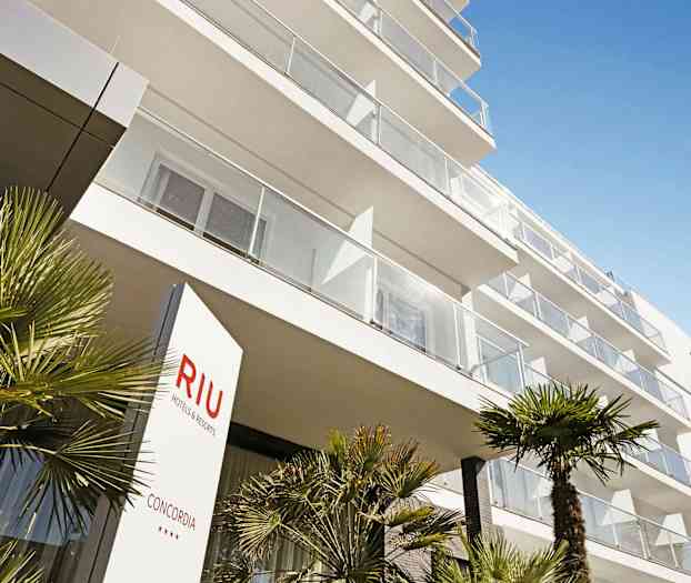 Moderni hotellirakennus parvekkeineen ja palmuja etualalla. (Tekoälyn luoma teksti)