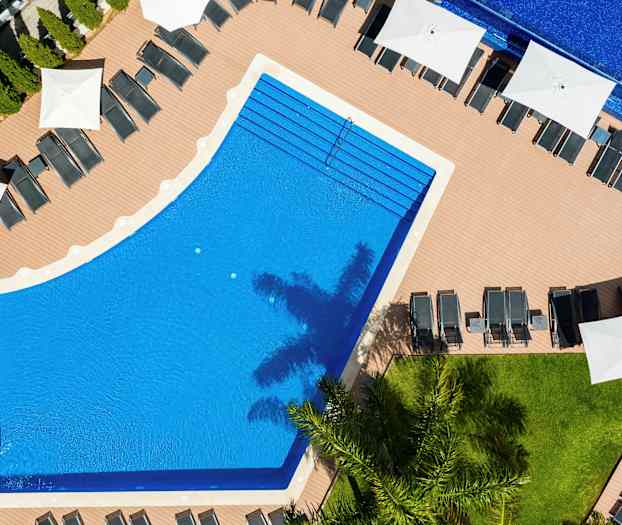 Ilmakuva uima-altaasta, jota ympäröivät aurinkotuolit ja aurinkovarjot. (Tekoälyn luoma teksti)