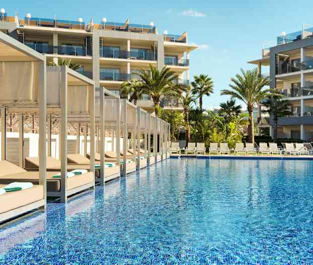 Ulkotila, jossa uima-allas, aurinkotuoleja ja hotellirakennuksia. (Tekoälyn luoma teksti)