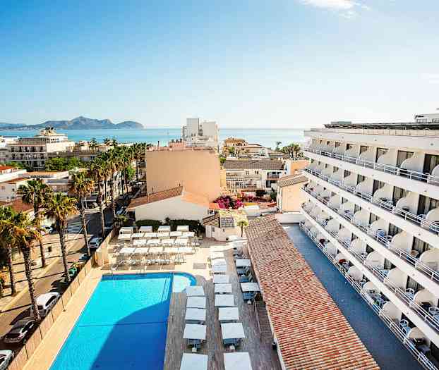 Ylhäältä katsottuna hotellin rakennus, uima-allas ja ympäröivä alue, taustalla meri. (Tekoälyn luoma teksti)