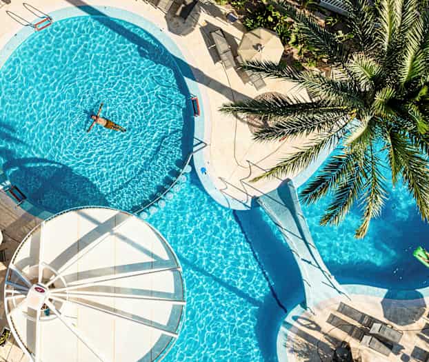 Ulkoallas, jota ympäröivät aurinkotuolit ja aurinkovarjot, yksi henkilö uimassa. (Tekoälyn luoma teksti)