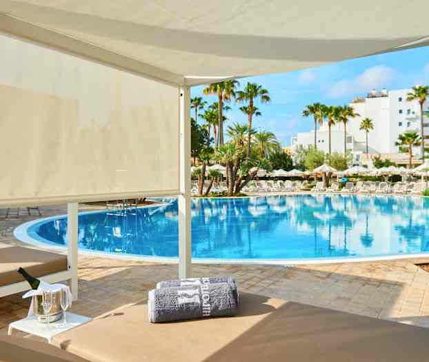 Ylellinen cabana uima-altaan äärellä, ympärillä palmuja ja aurinkovarjoja. (Tekoälyn luoma teksti)