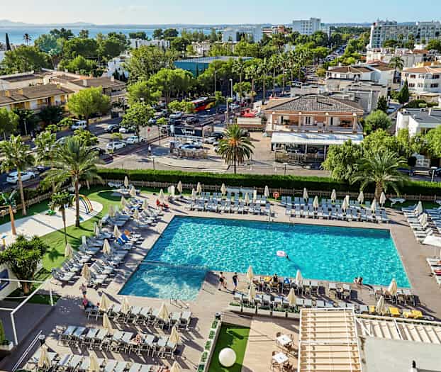 Uima-allas, jota ympäröivät aurinkotuolit, ympäröivää vehreyttä ja rakennuksia taustalla. (Tekoälyn luoma teksti)