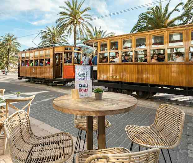 Puinen raitiovaunu ohittaa aukion, jossa on pöytiä ja tuoleja. (Tekoälyn luoma teksti)