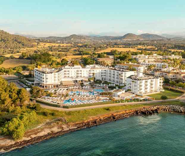 Ilmakuva hotellikompleksista, jota ympäröivät vehreys ja vesi. (Tekoälyn luoma teksti)