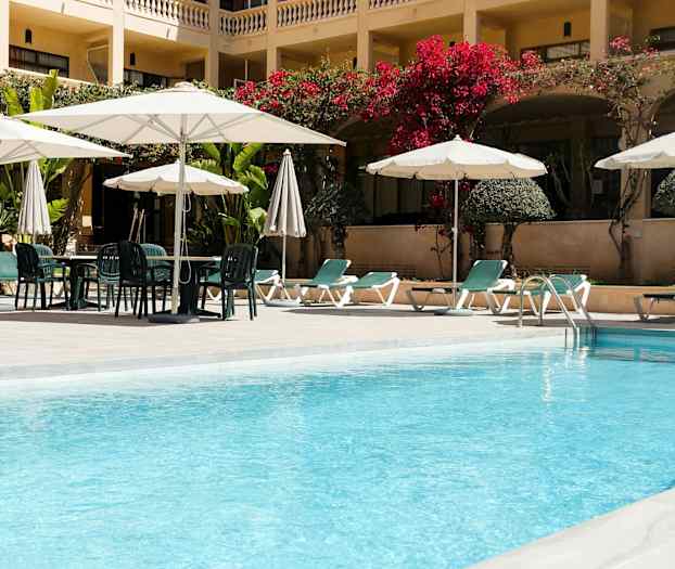 Hotellin uima-allas aurinkotuoleilla ja aurinkovarjoilla. (Tekoälyn luoma teksti)