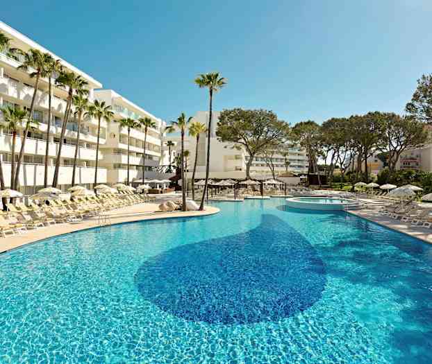 Aurinkoinen uima-allas, jota ympäröivät aurinkotuolit, aurinkovarjot ja palmut hotellin vieressä. (Tekoälyn luoma teksti)