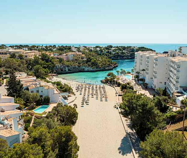 Ranta aurinkovarjoineen, jota ympäröivät rakennukset ja kasvillisuus, taustalla meri. (Tekoälyn luoma teksti)