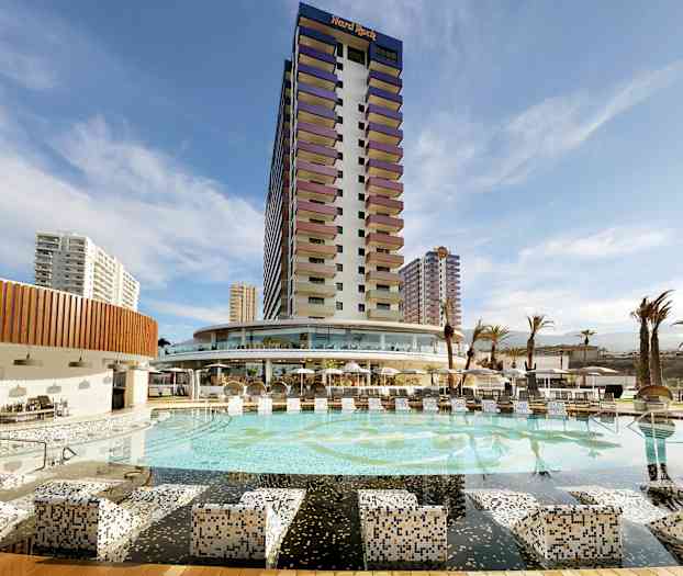 Hotelli, jossa on suuri uima-allas ja ympäröiviä rakennuksia sinisen taivaan alla. (Tekoälyn luoma teksti)