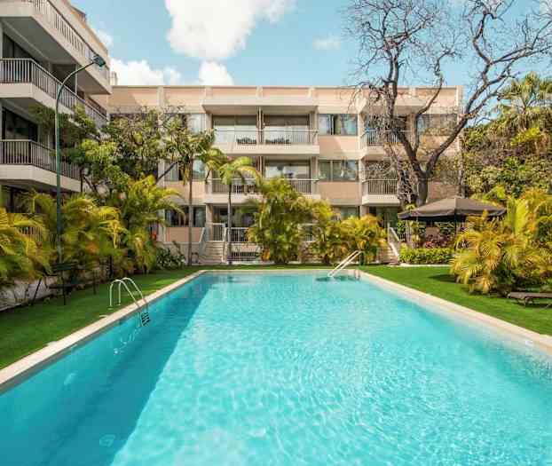 Ulkouima-allas, jota ympäröivät palmut ja parvekkeellinen rakennus. (Tekoälyn luoma teksti)