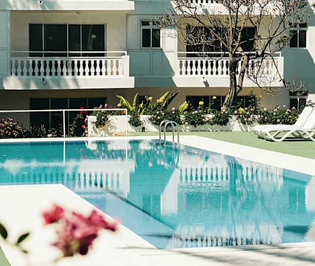 Ulkoallas aurinkotuoleilla valkoiseksi maalatun hotellin vieressä. (Tekoälyn luoma teksti)